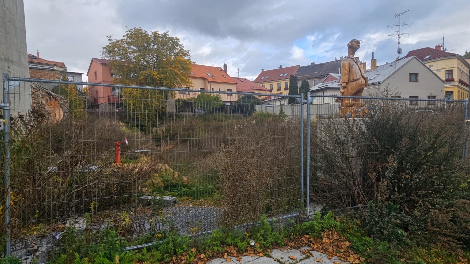 Oplocený prázdný pozemek v zástavbě — místo, kde dříve stály domy